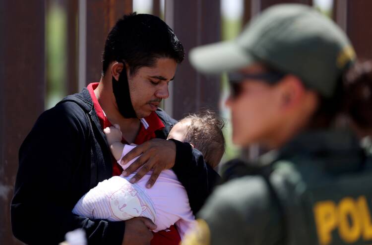 A man from Brazil holds his 9-month-old daughter in Andrade, Calif., April 19, 2021, as they wait to be transported by Border Patrol after crossing into the United States from Mexico. (CNS photo/Jim Urquhart, Reuters)