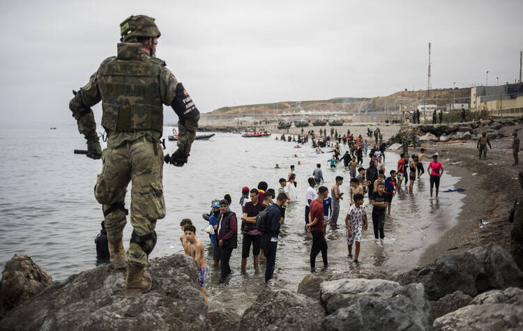 People mainly from Morocco stand on the shore as the Spanish Army cordons off a beach at the border of Morocco and Spain in the Spanish enclave of Ceuta on May 18. Ceuta faced a humanitarian crisis after thousands of Moroccans took advantage of relaxed border control in their country to swim or paddle in inflatable boats into European soil. (AP Photo/Javier Fergo)