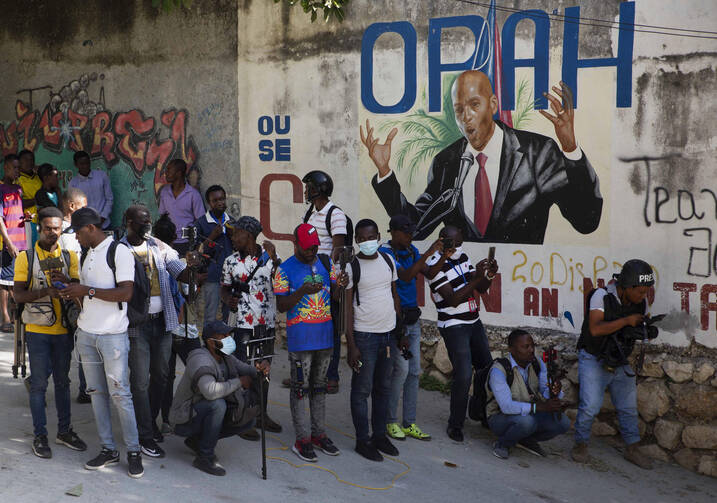 Journalists gather near a mural featuring Haitian President Jovenel Moise, near the leader’s residence where he was killed by gunmen in the early morning hours, and his wife was wounded, in Port-au-Prince, Haiti, Wednesday, July 7, 2021. (AP Photo/Joseph Odelyn)