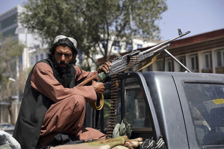 A Taliban fighter sits on the back of a vehicle with a machine gun in front of the main gate leading to the Afghan presidential palace, in Kabul, Afghanistan