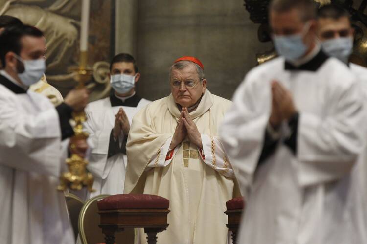 Cardinal Burke processes into Mass without a face mask, surrounded by acolytes.