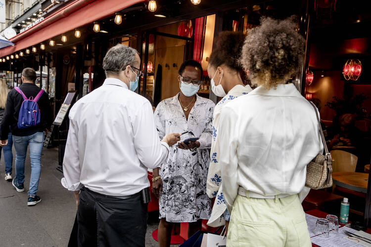 Women show their health passes to a waiter in Paris on Aug. 19, 2021. France, Italy, Denmark and the U.S. cities of New York, San Francisco and New Orleans are among the places that have imposed vaccination requirements at places like restaurants, gyms and theaters as the Delta variant of Covid-19 spreads. (AP Photo/Adrienne Surprenant)