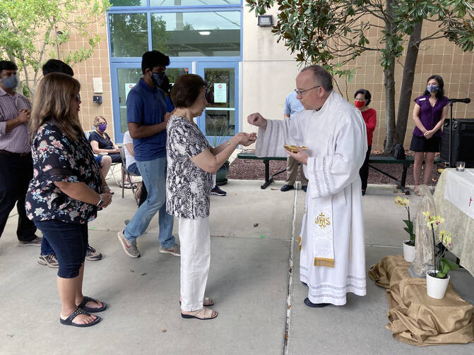 The parish priest distributes Communion to parishioners outside a building.