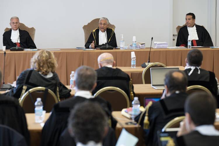 The judges of the Vatican City State criminal court—Venerando Marano, Giuseppe Pignatone and Carlo Bonzano—sit at a long table with a brown tablecloth in a makeshift court room.