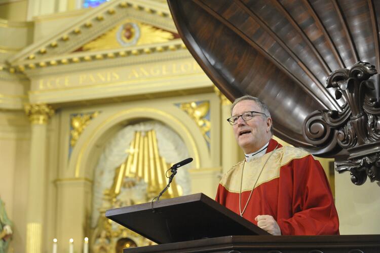 Bishop Robert Barron, in a red chasuble, stands at the pulpit at St. Louis Cathedral in New Orleans.