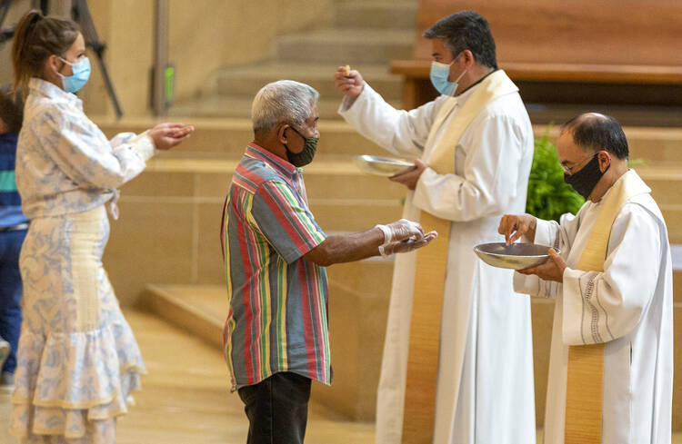 The faithful wear masks and some wear gloves as they receive Communion at the first English Mass with faithful present at the Cathedral of Our Lady of the Angels in downtown Los Angeles.