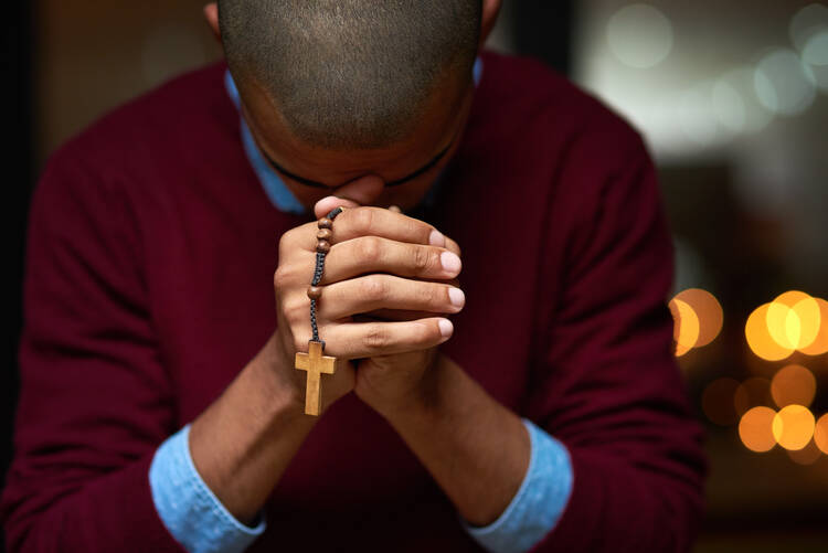 A man bows his head in prayer, clasping the rosary between his hands
