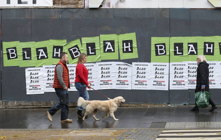 People walk past posters placed by climate activists ahead of a protest march in Glasgow, Scotland, on Nov. 5, 2021. (AP Photo/Scott Heppell)