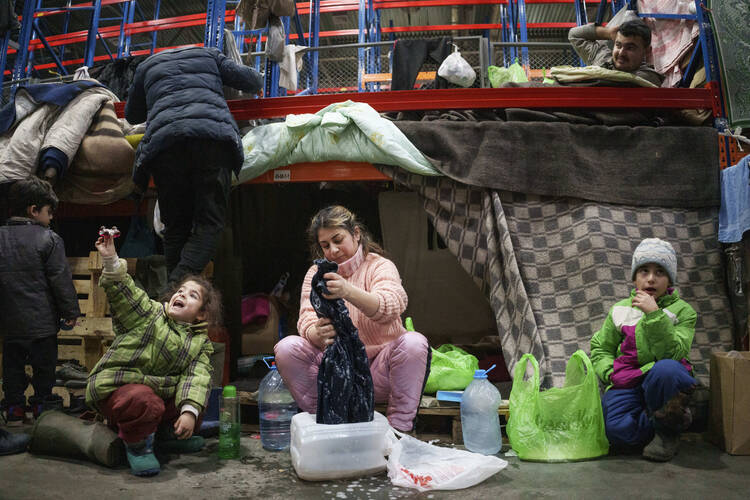 A woman washes clothes as migrants settle at the Bruzgi checkpoint center at the Belarus-Poland border near Grodno, Belarus, on Dec. 23, 2021. Since Nov. 8, a large group of migrants, mostly Iraqi Kurds, has been stranded at the border crossing with Poland. (AP Photo/Pavel Golovkin)