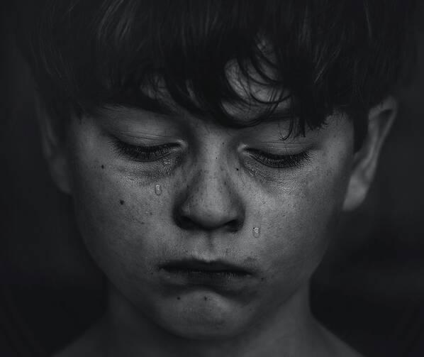 Black-and-white photo of a boy with a tear running down his cheek.
