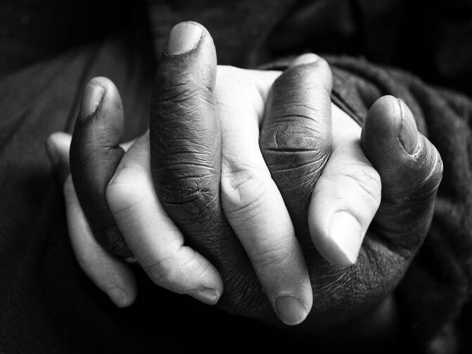 Two people, one white and another Black, holding hands.