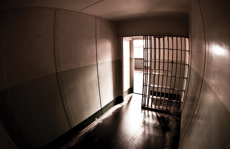 Stock photo of an empty prison cell with the door slightly open.