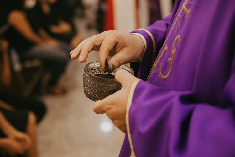 A priest in a purple alb collects ashes on his fingers for Ash Wednesday.