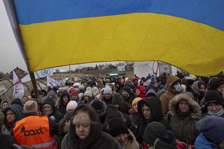 A Ukrainian volunteer Oleksandr Osetynskyi, 44 holds a Ukrainian flag and directs hundreds of refugees after fleeing from the Ukraine and arriving at the border crossing in Medyka, Poland, Monday, March 7, 2022. (AP Photo/Visar Kryeziu)