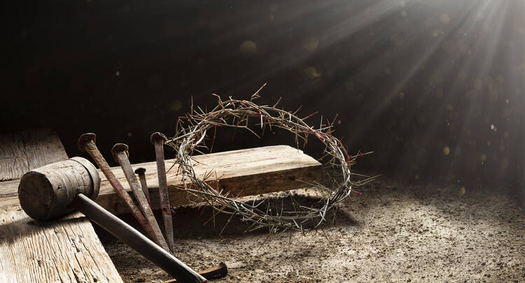 A crown of thorns and three nails rest on the edge of a wooden cross.