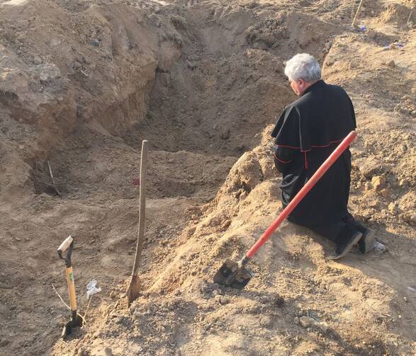 Cardinal Konrad Krajewski, the papal almoner, who is in Ukraine as a papal envoy, prays over a mass grave near Borodyanka, Ukraine, April 15, 2022. (CNS photo/Vatican Media)