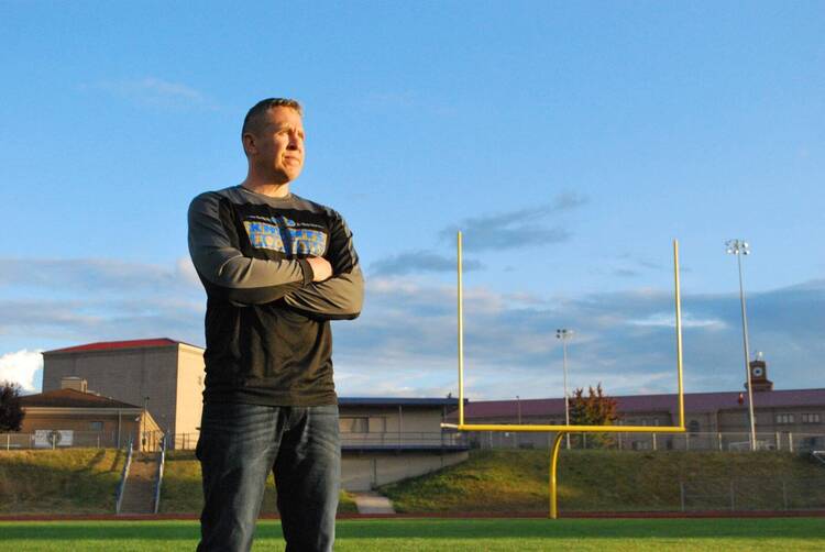 Joe Kennedy standing with crossed arms in front of a football field.