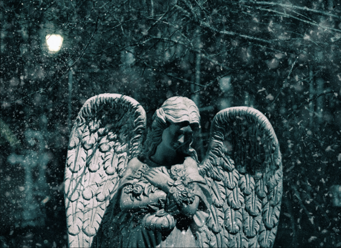 Stock image of a stone statue of an angel surrounded by falling snow.