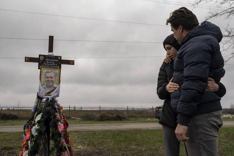 Yura Nechyporenko, 15, hugs his uncle Andriy Nechyporenko above the grave of his father Ruslan Nechyporenko at a cemetery in Bucha, on the outskirts of Kyiv, Ukraine, on April 21, 2022. The teen survived an attempted killing by Russian soldiers while his father was killed. (AP Photo/Petros Giannakouris)