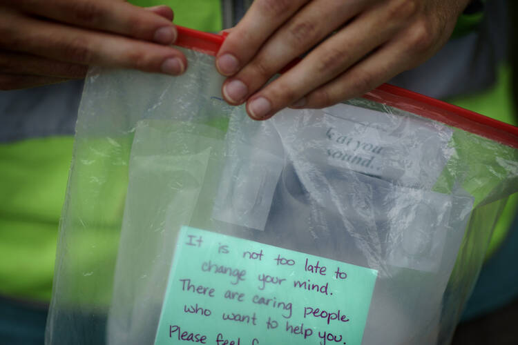 A person in a neon traffic vest holds a ziploc bag containing a note which reads, "it is not too late to change your mind."