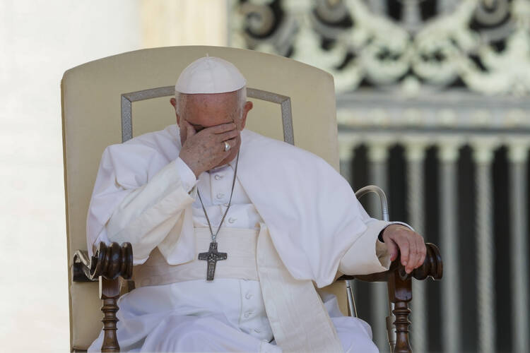 Pope Francis, seated, presses his hand against his face