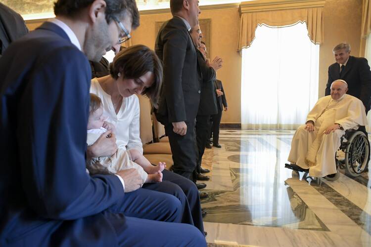 The pope in a wheelchair greets a crowd and a baby