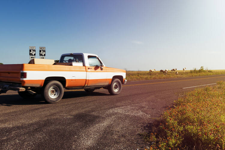 Stock photo of a red pickup truck driving down a dusty road in late afternoon.