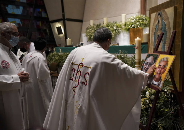A priest touches the photos of Jesuit priests Javier Campos Morales, left, and Joaquin Cesar Mora Salazar during a Mass to mourn their death, at a church in Mexico City, on June 21, 2022. (AP Photo/Fernando Llano)