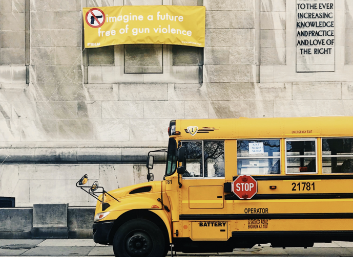 A school bus in front of a building; the building has a yellow banner on it that says “imagine a future free of gun violence.”