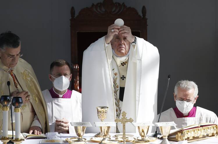 Pope Francis, flanked by three priests, somberly elevates the Eucharist