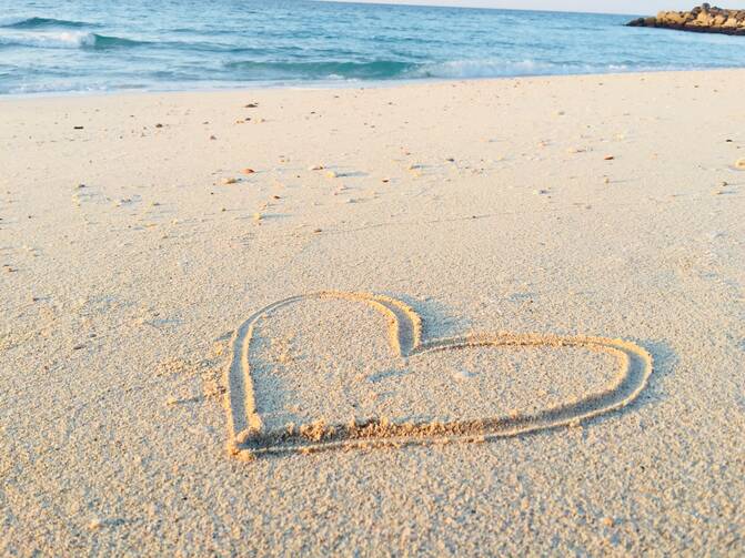 A heart drawn in the sand next to the water on a beach.
