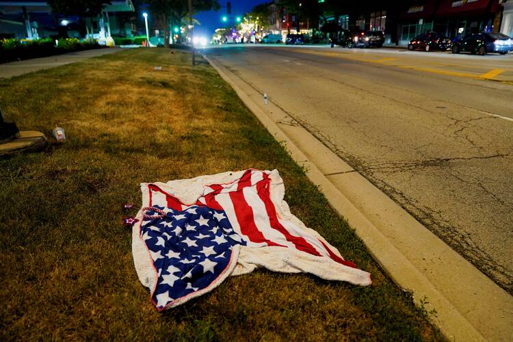 A lawn towel with the image of the American flag lies abandoned on a stretch of grass next to a road.