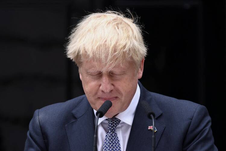 Boris Johnson stands before a microphone with his head bowed