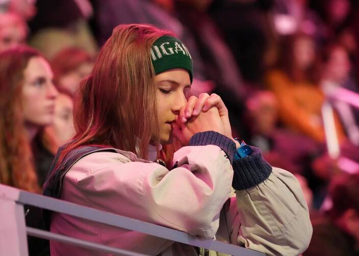 A young woman rests her forehead on her clasped hands