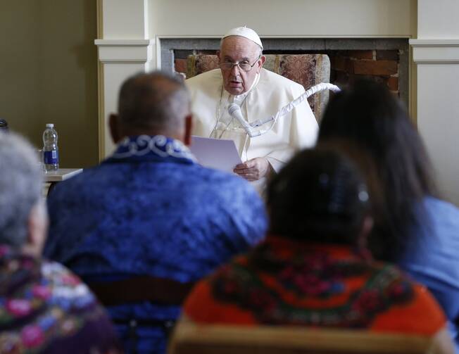 The pope, seated, speaks to a crowd