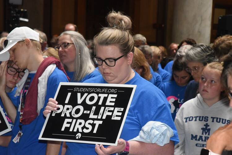 In the midst of a crowd, a woman holds a sign which says "I vote pro-life first."