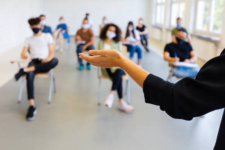 A stock photo of a teacher's hands in a classroom with some students.