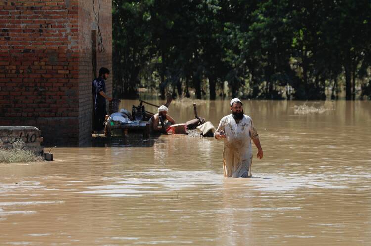 A man wades through floodwaters trying to salvage his belongings following heavy rains during the monsoon season in Charsadda, Pakistan, Aug. 28, 2022. (CNS photo/Fayaz Aziz, Reuters)