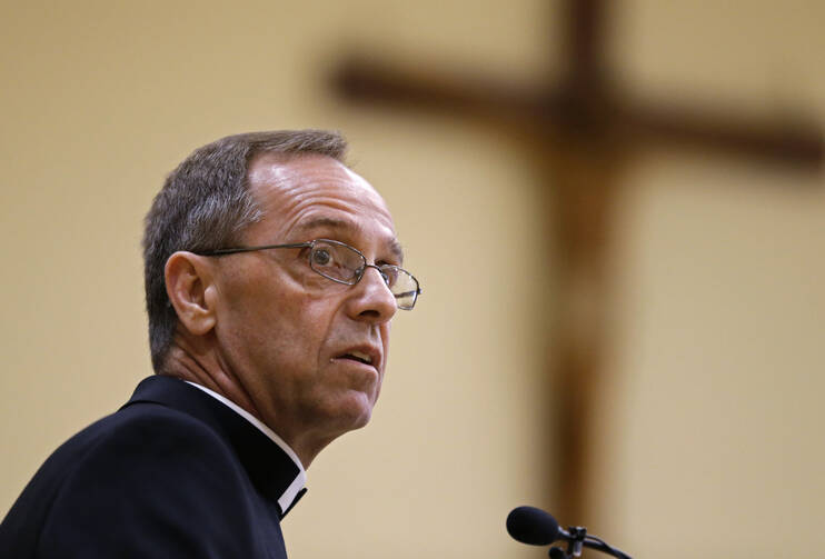 bishop charles thompson talks at a microphone with a crucifix in the background