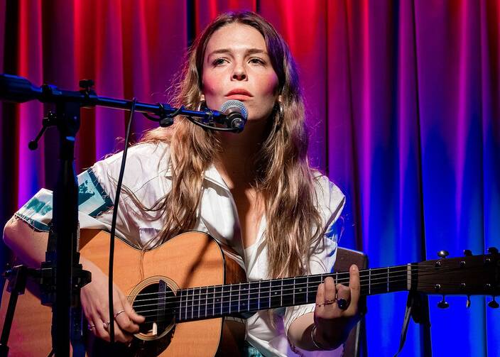 Maggie Rogers plays a guitar in front of a microphone
