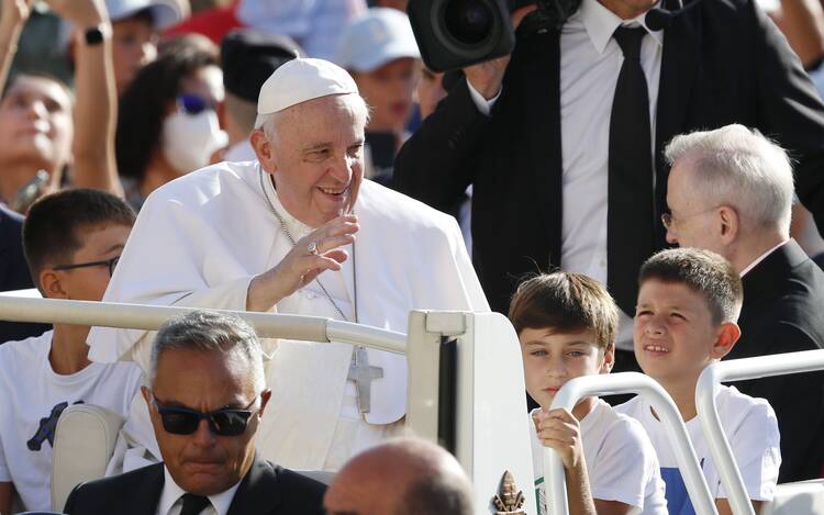 pope francis waves to the crowd from the popemobile. children are seated behind him smiling