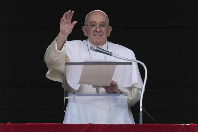Pope Francis stands at a podium, waving towards the camera