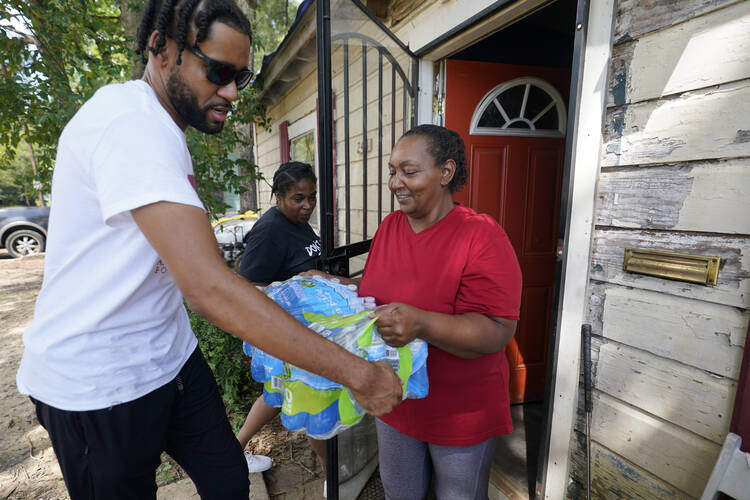 Jeremy Myers, left, of the Aids Healthcare Foundation delivers water to Shaun Brown in Jackson, Miss., Thursday, Sept. 1, 2022. A recent flood worsened Jackson's longstanding water system problems. (AP Photo/Steve Helber)