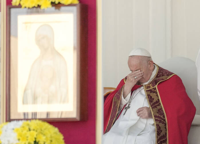Pope Francis, seated and dressed in red priests clothing, covers his eyes 