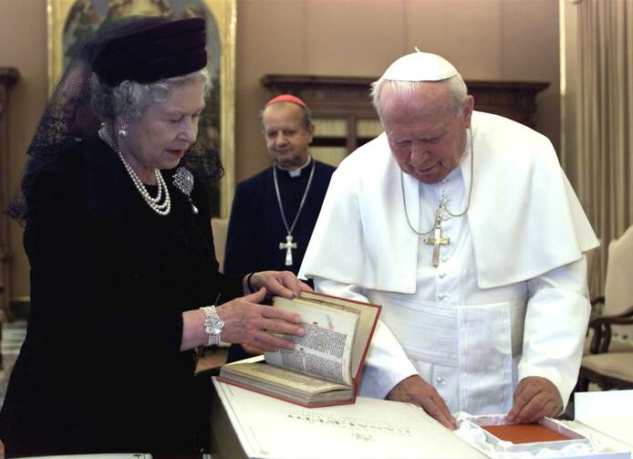 Queen Elizabeth II, dressed in black, opens a book alongside Pope John Paul II