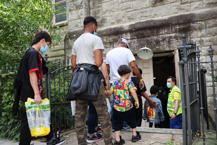 people stand backs facing the camera, outside a church. some are young children and they carry bags