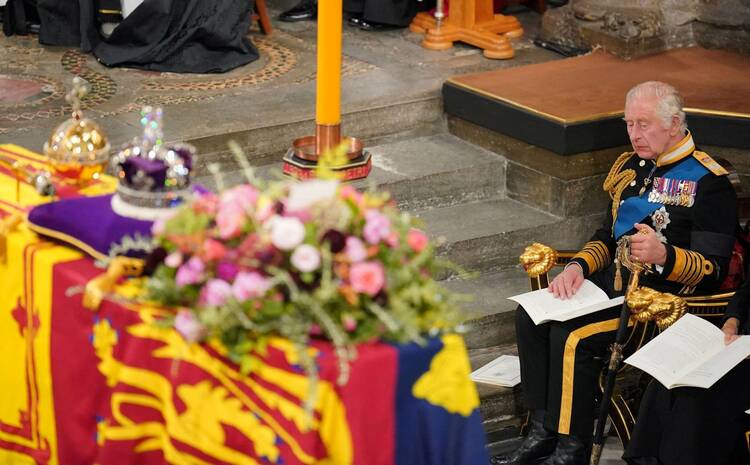 King Charles III sits in front of a coffin dressed in a military uniform