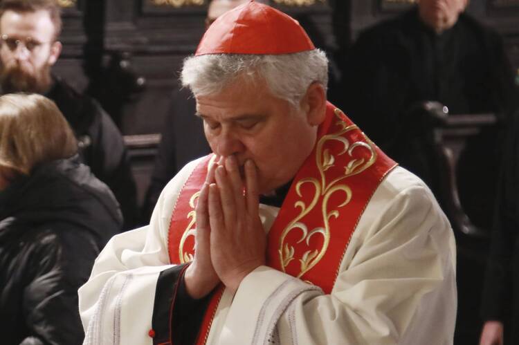 cardinal konrad krajewski wearing his red hat and red stoll praying