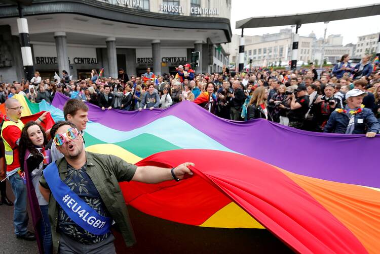 people standing around a large pride flag of many colors in belgium in may 2018