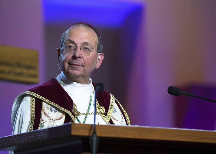 archbishop william lori of baltimore stands at a lectern and talks wearing vestments that are white and red